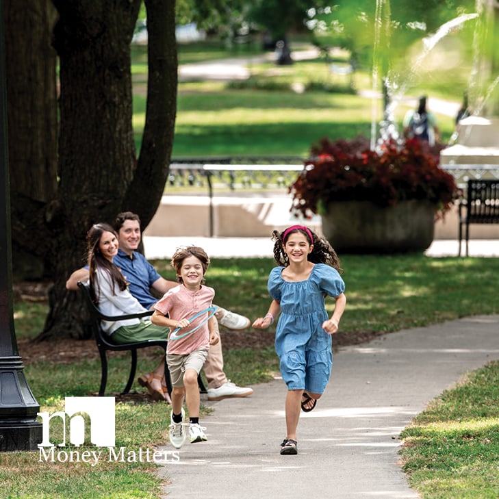 A couple sit on a bench, watching two children running.