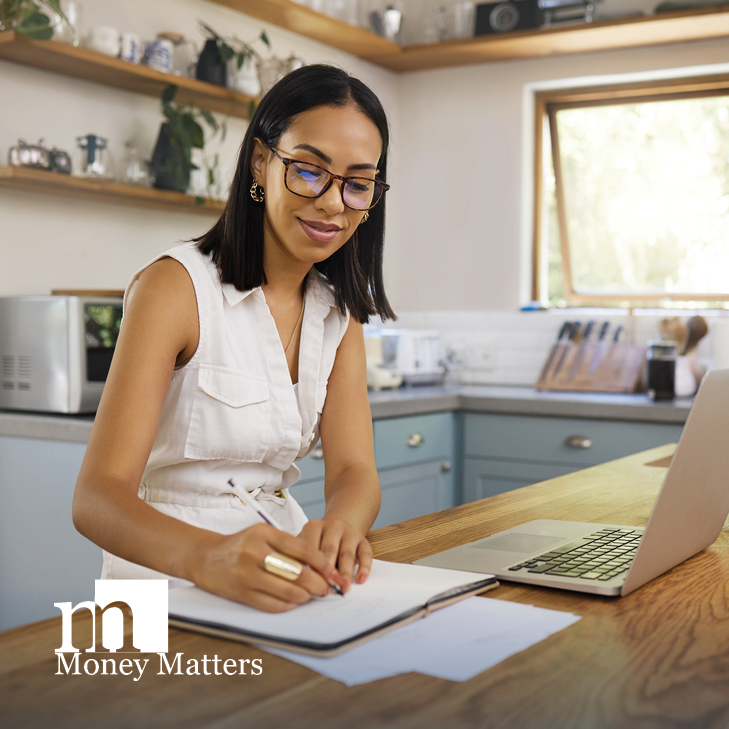 A woman sits in a kitchen with a laptop on the counter.