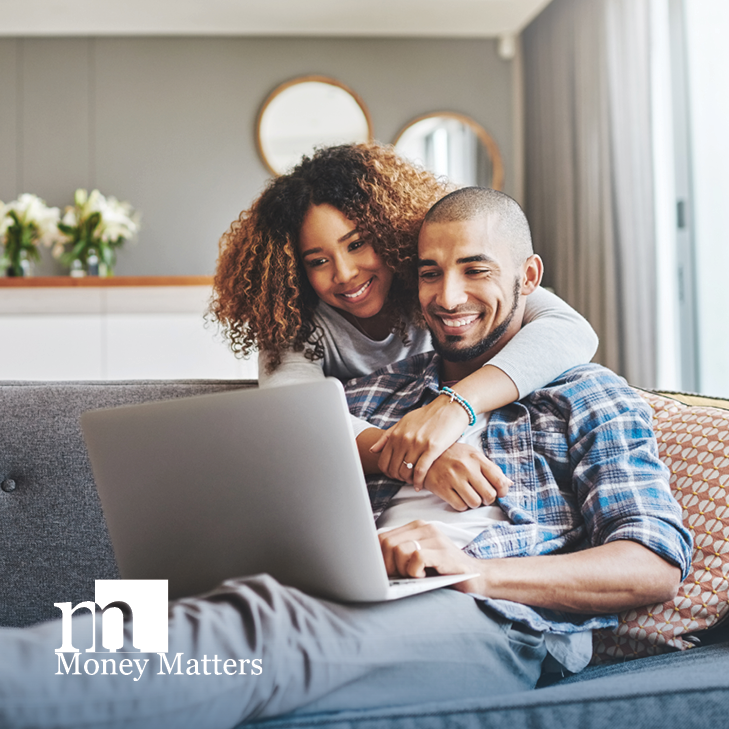A woman hugs a man as they look at a laptop.