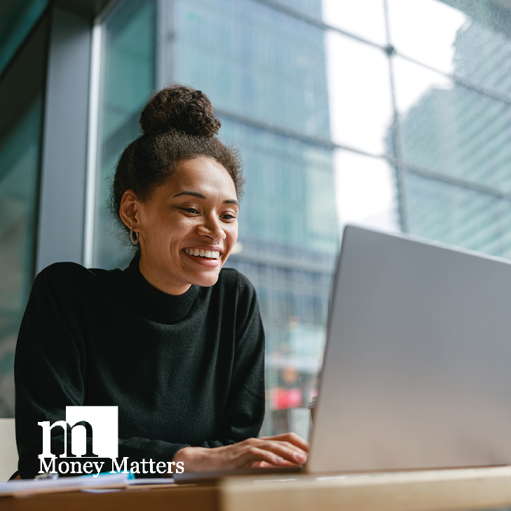 A woman sits at a desk, looking at her laptop.