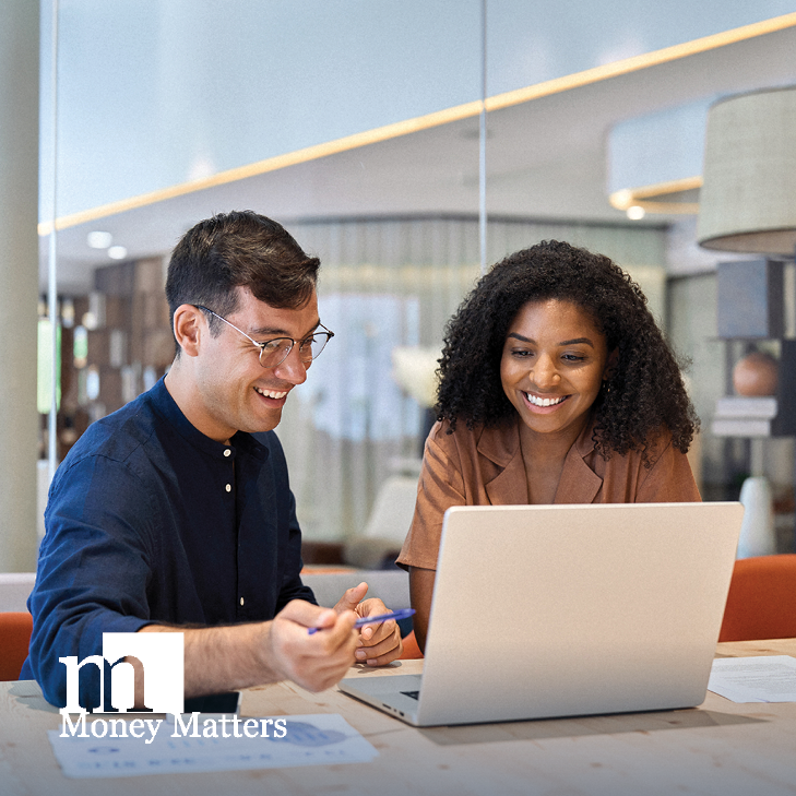 A man and woman sit at a conference room table, looking at a laptop