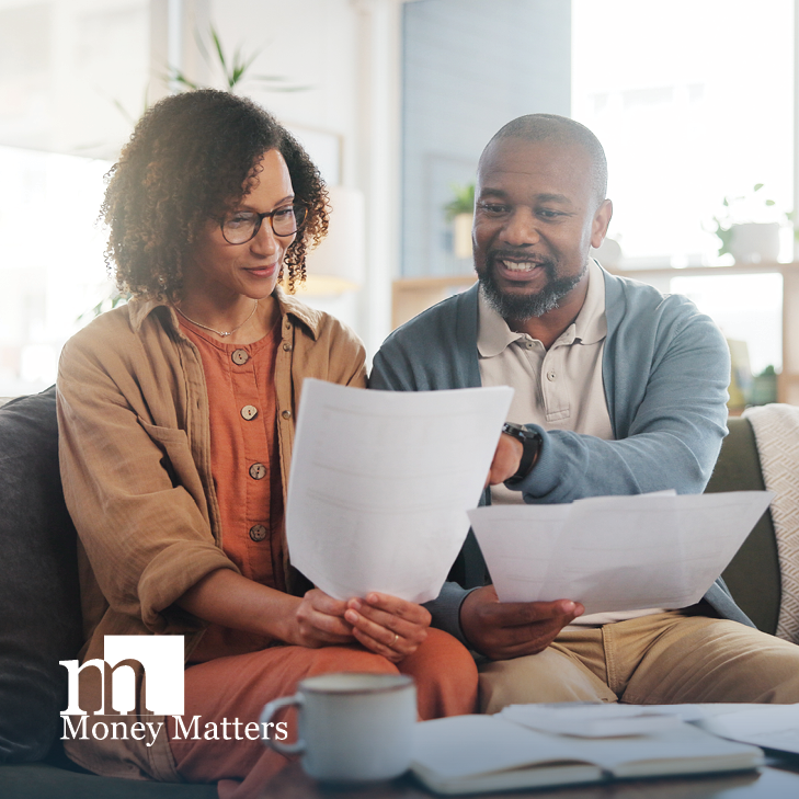 A man and woman sit on a couch, looking at paperwork.