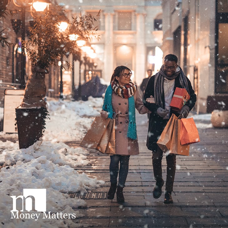 A man and woman walk in the snow, holding shopping bags